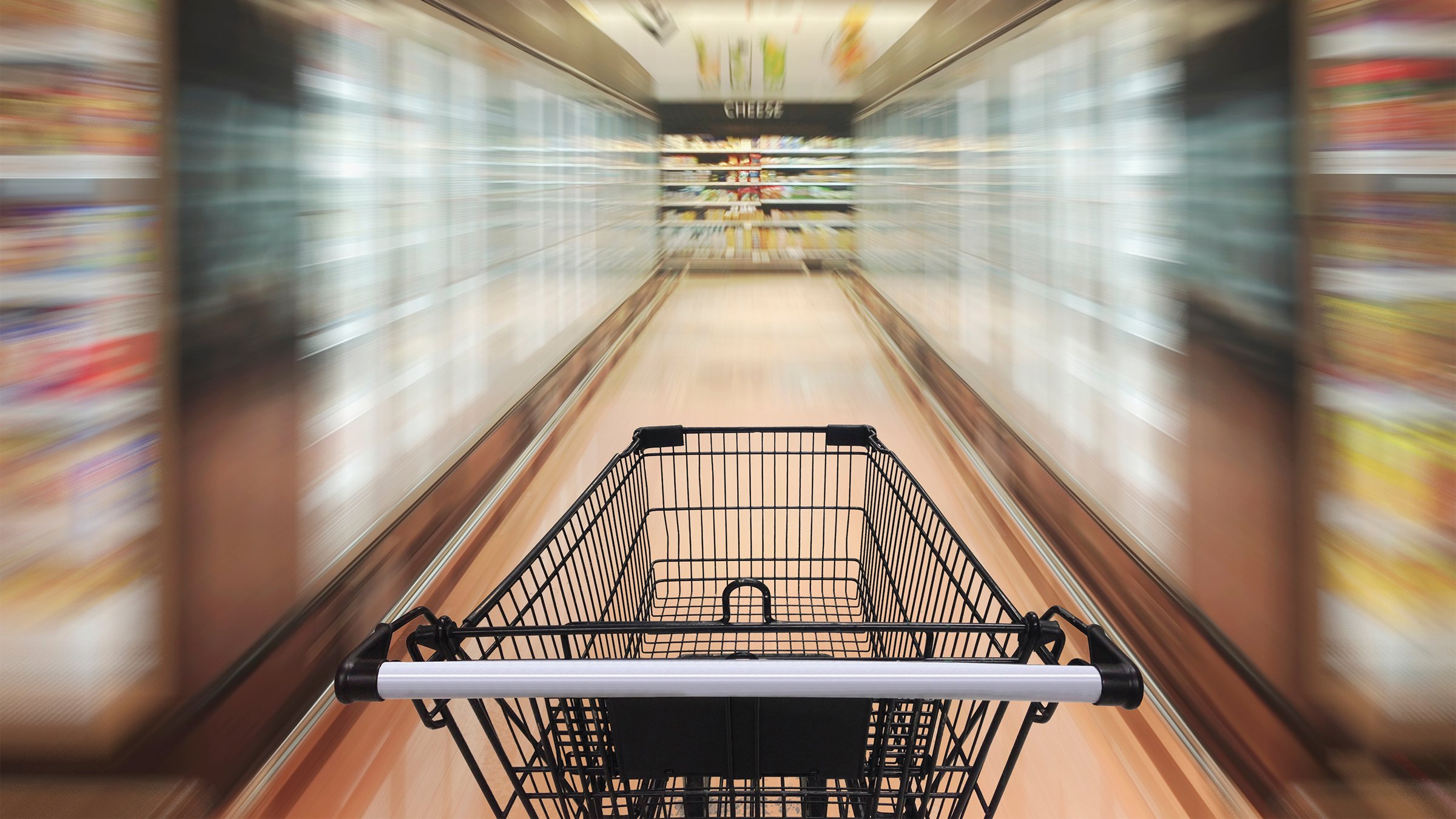 Empty shopping cart in blurred supermarket aisle.