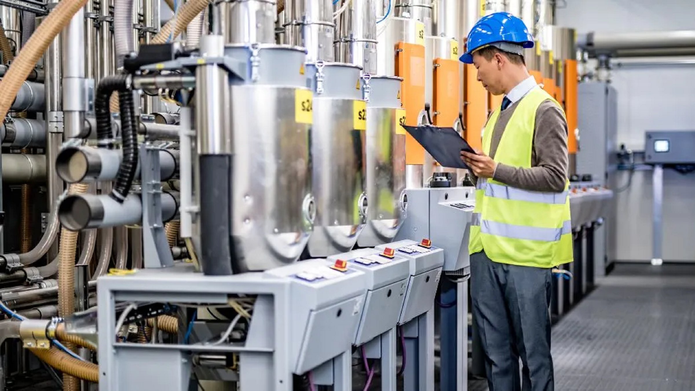 Male engineer with clipboard examining manufacturing machinery in factory.