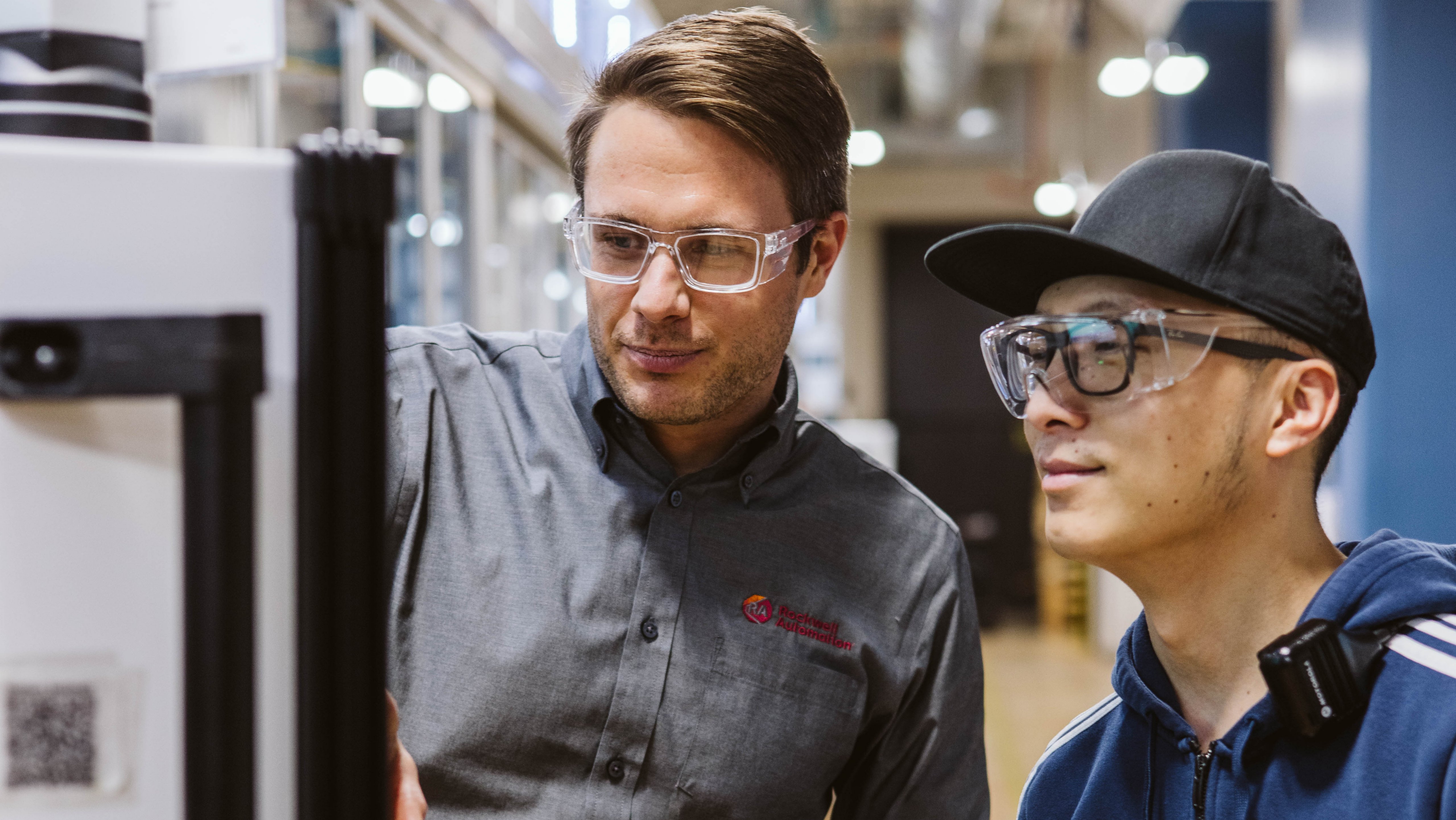 Engineer in safety glasses explaining equipment to a colleague during a training session in a manufacturing facility.