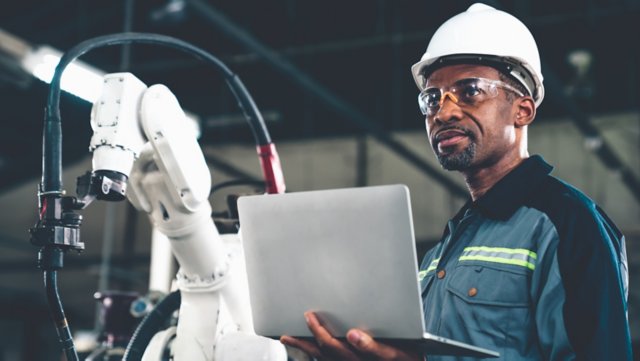 African American factory worker working with adept robotic arm in a workshop . Industry robot programming software for automated manufacturing technology .