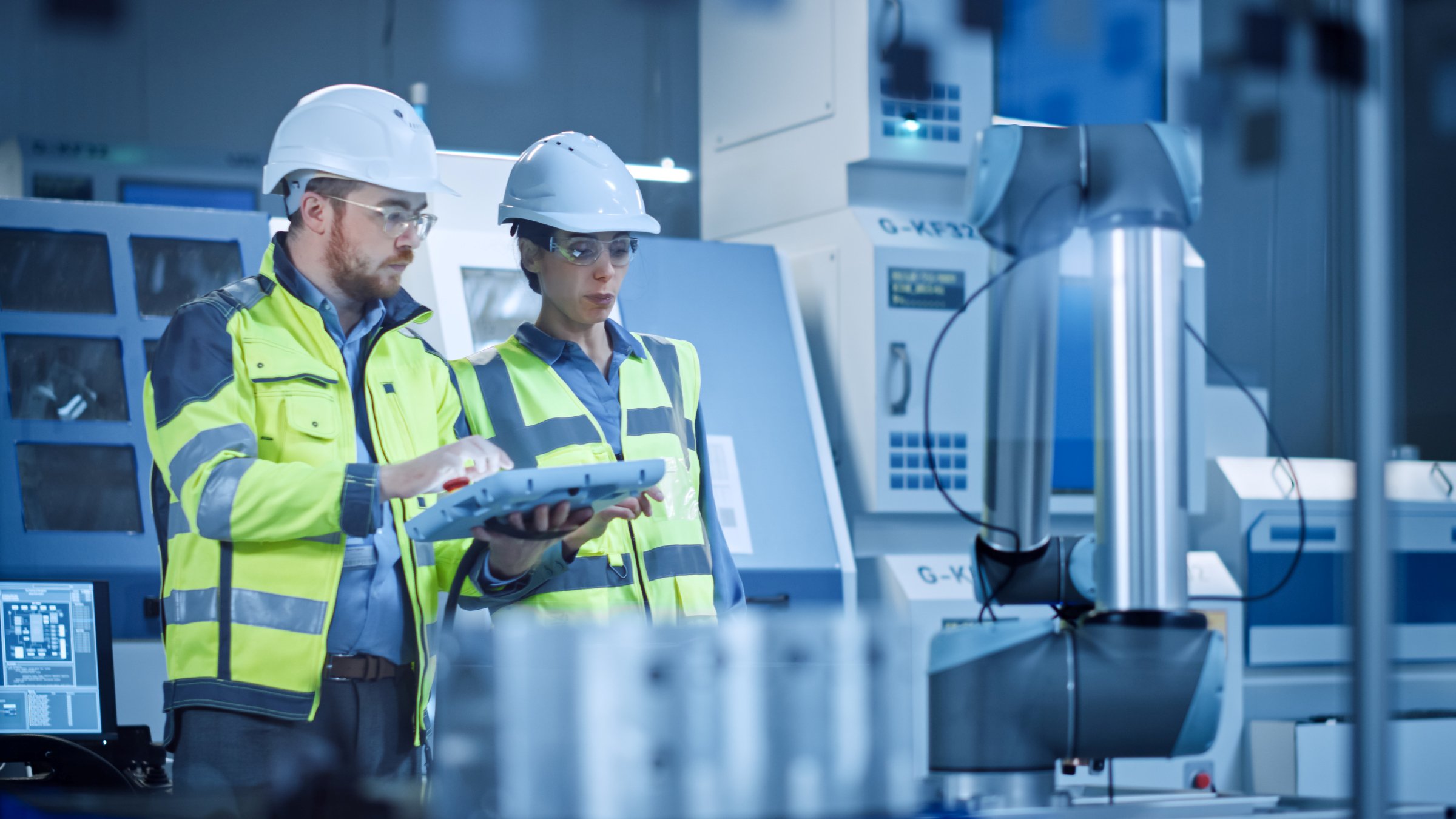 Factory Workshop: Professional Female Engineer, Male Machinery Operator Use Industrial Digital Tablet Computer to Work and Program Robot Arm for Production Line. High-Tech Facility with CNC Machines