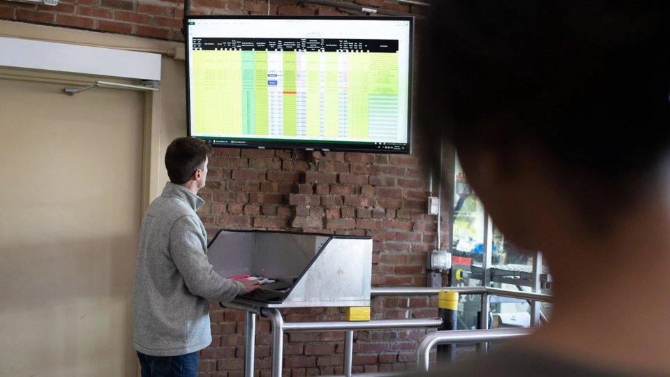 A man in a process industry factory looks up at a FactoryTalk AssetCentre display on an overhead TV.