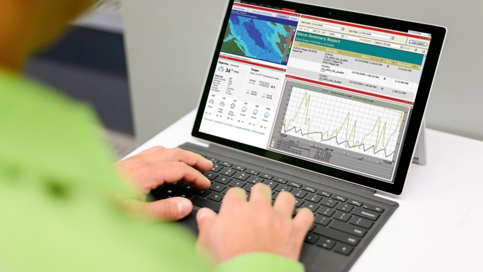 Looking over the shoulder of a person with a green work shirt as they type on a PC and look at a FactoryTalk Historian screen.