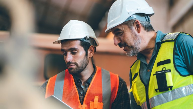 Teamwork men in construction site, Two civil engineer or professional foreman in safety helmet hard hat using blueprint in digital tablet working while standing at industrial factory, teamwork concept