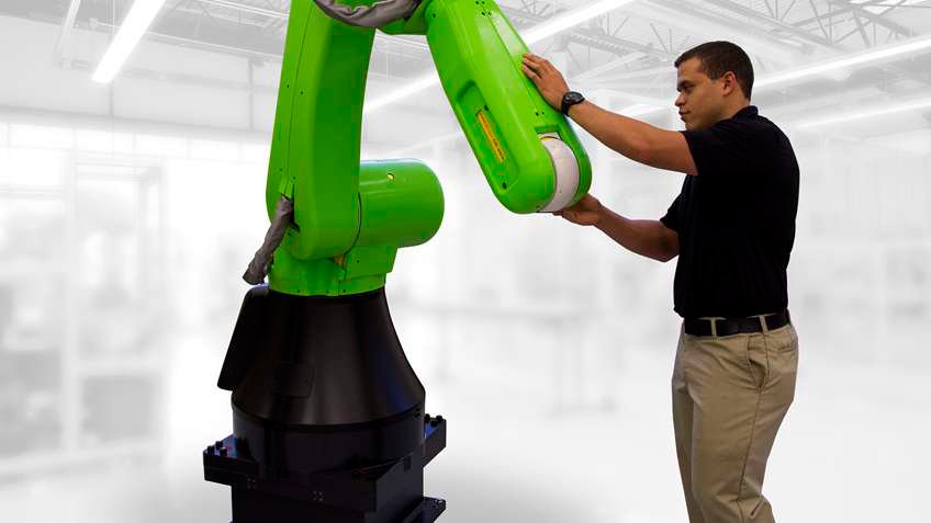 Man inspecting the exterior of a green collaborative robot arm while standing