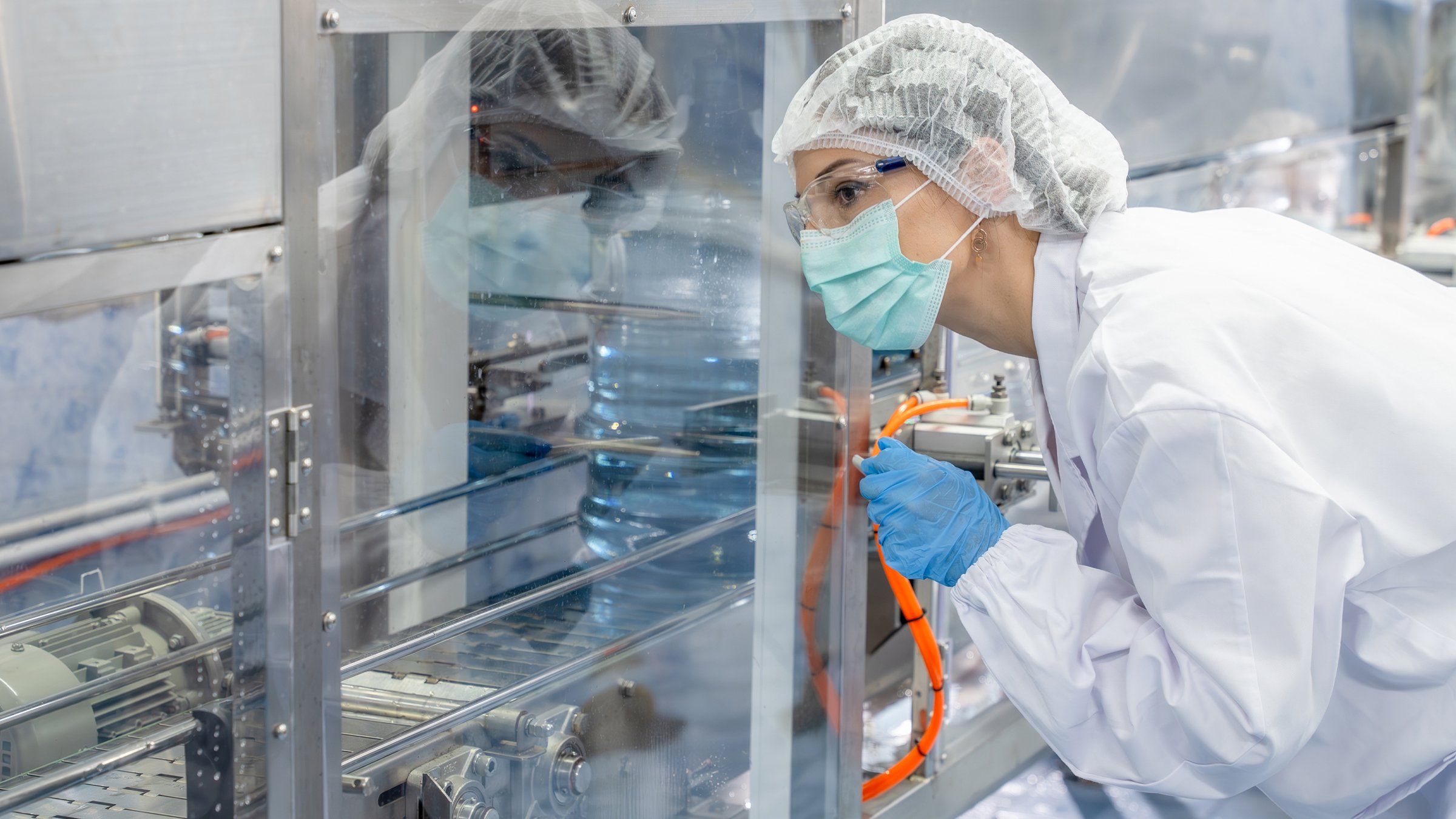Female Caucasian scientist worker, holding clipboard tablet, checking the quality of water filling machine in the factory