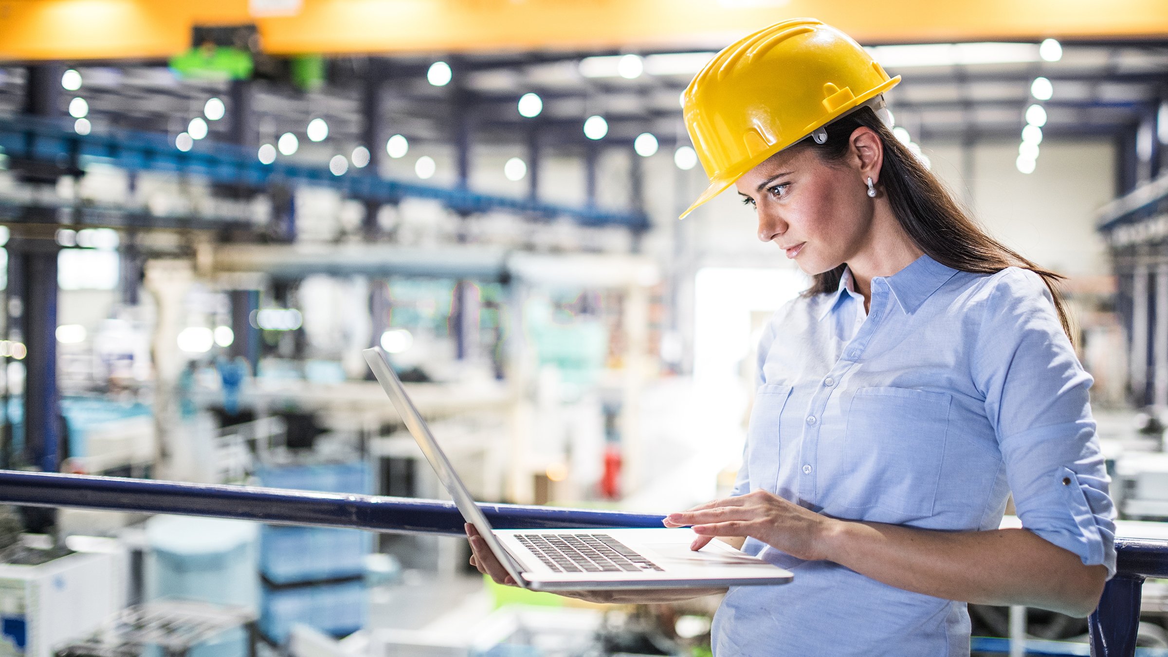 A female project manager in yellow hard hat stands in a modern factory while assessing functional safety requirements using a laptop computer. The Safety Functional Requirements Specification (SFRS) is the second step of the safety lifecycle and directly impacts the design and validation of the control system.