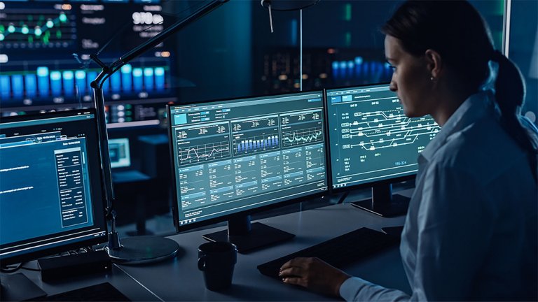 Female software engineer sitting in front of computers monitoring manufacturing big data. 