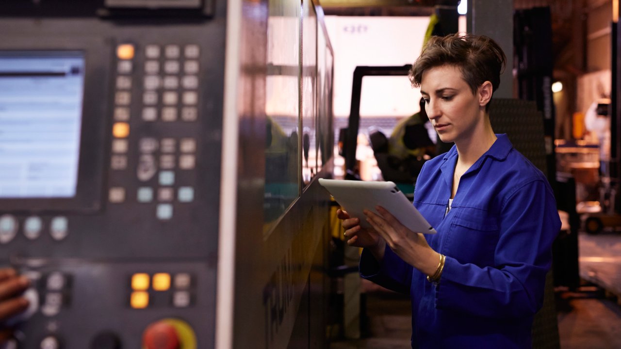 Female steel worker standing next to laser cutting machine holding tablet inside factory