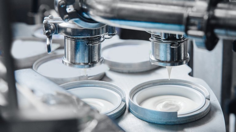 Automated machine filling yoghurt into packages at food production plant. 