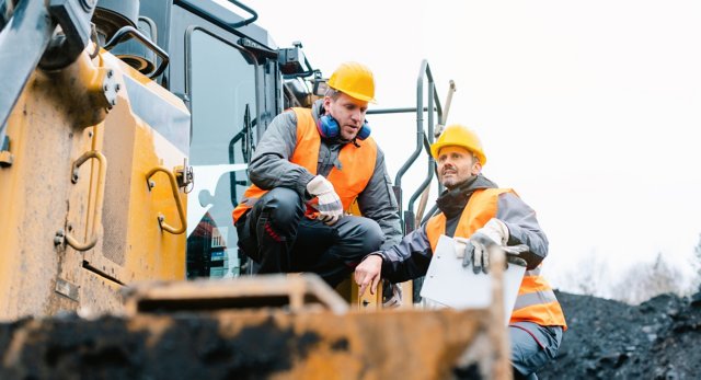Foreman showing worker in open-cast mining pit direction with arm stretched