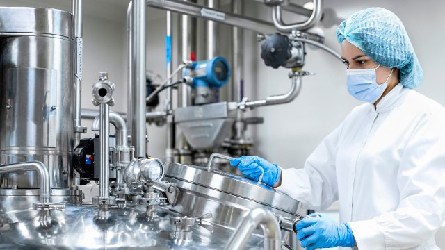 Fully equipped woman seen holding a machine in a laboratory of pharmaceutical industry