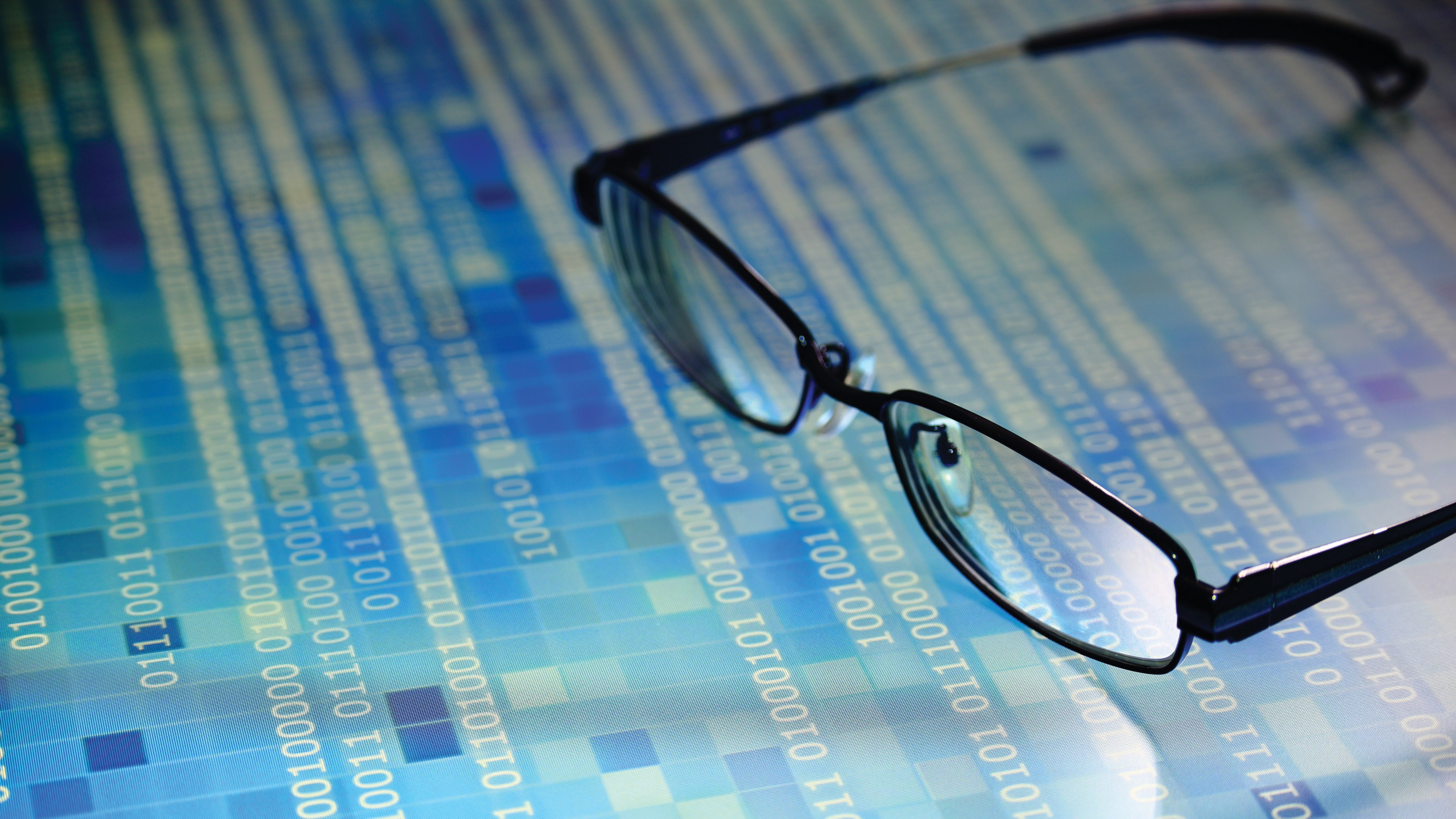 big data analysis. glasses placed on a LED digital panel display white light one and zero binary text number in moving motion pattern. modern technology blue block grid pattern backgrounds