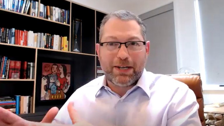 Grant Geyer, Chief Product Officer at Claroty, wearing white button up shirt and glasses with bookcases in the background.