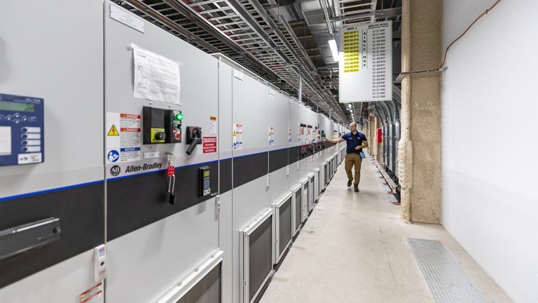 Engineer inspects a long lineup of dozens of tall, grey industrial-sized variable frequency drives (VFDs).