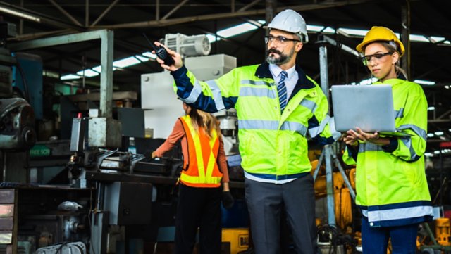 Industrial engineer in suite and safety helmet working in factory, holding a tablet concerned with OT cybersecurity trends.