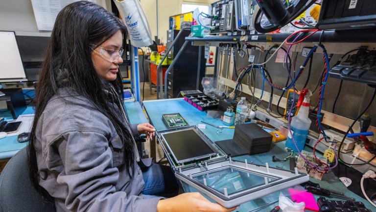 A female Rockwell Automation remanufacturing technician in gray lab coat replaces the screen and performs validation on an Allen-Bradley® PanelView™ HMI product.