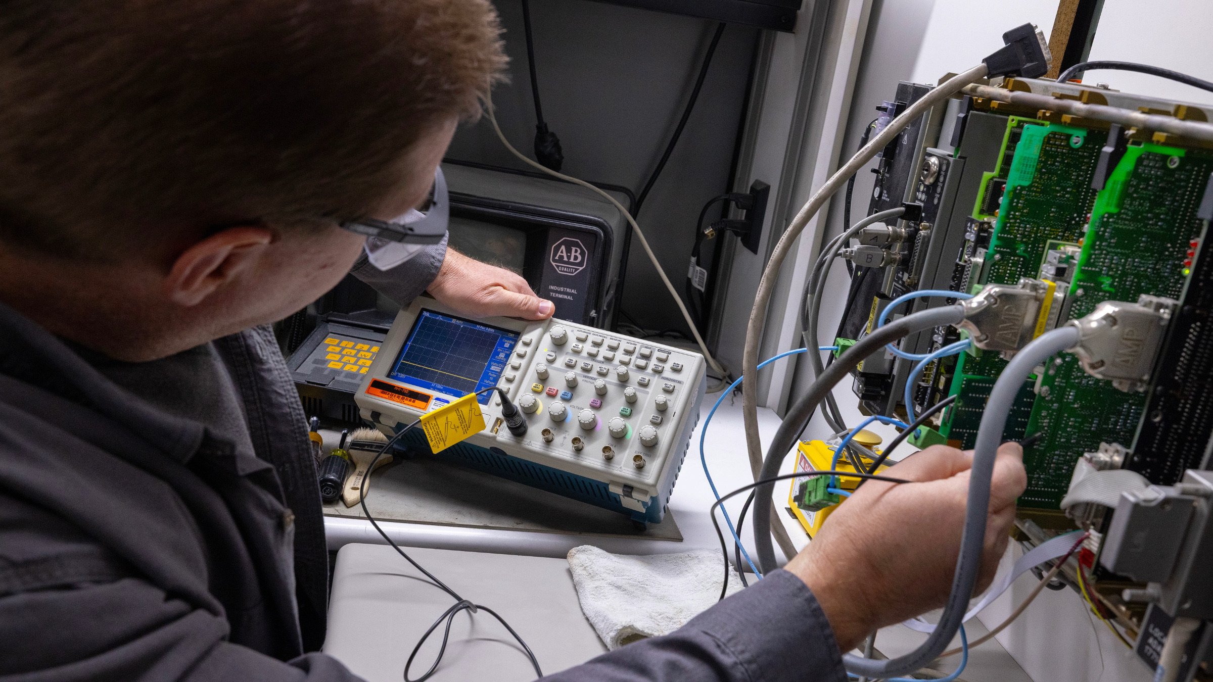 A Rockwell Automation remanufacturing technician uses an oscilloscope to functionally test a discontinued Allen-Bradley® PLC-5® programmable controller in a validated test environment. He is testing the wave form of the power coming in and out using the original test fixture used to manufacture the product in the 1990s, to ensure proper firmware updates and OEM components.