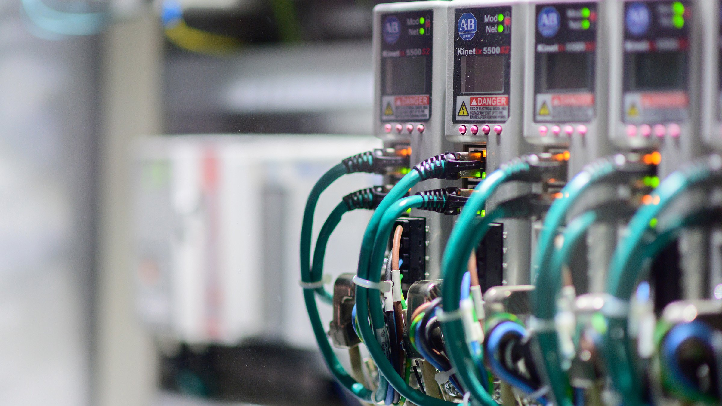 A row of four Kinetix 5500 servo drives powered on and connected by blue ethernet cables. 