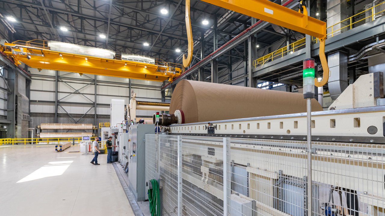 A large roll of brown kraft paper on a winding machine has fixed guarding to keep employees safe.