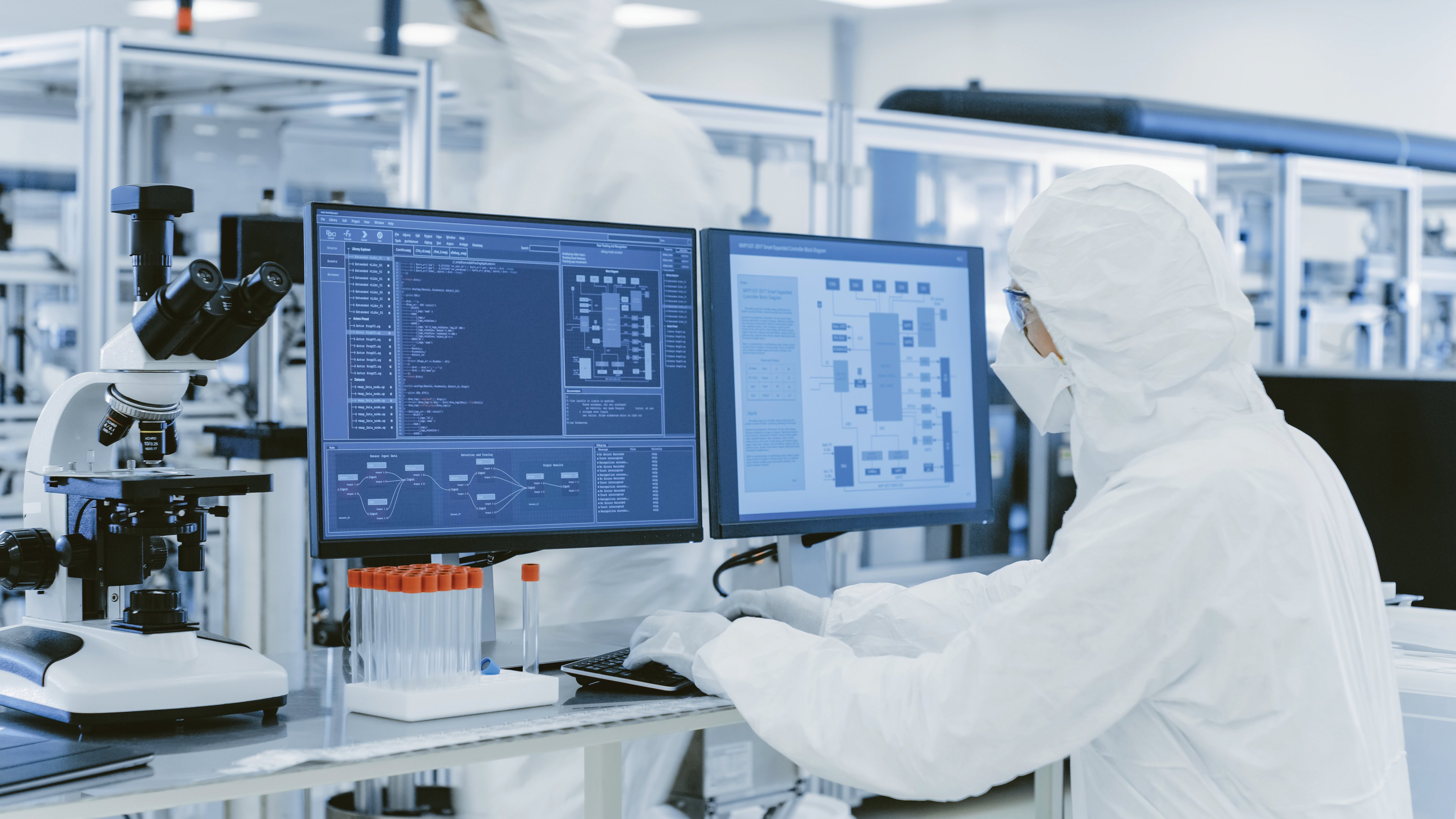 In Laboratory Over the Shoulder View of Scientist in Protective Clothes Doing Research on a Personal Computer. Modern Manufactory Producing Semiconductors and Pharmaceutical Items.