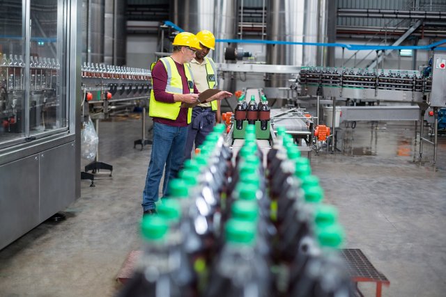 Two factory workers monitoring cold drink bottles on production line at drinks production plant