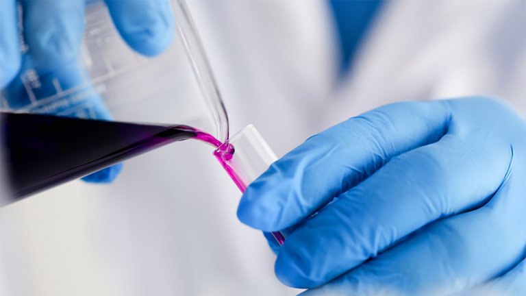 Male chemist holds glass test tube overflowing with liquid potassium permanganate solution for an analysis reaction for chemical manufacturing.