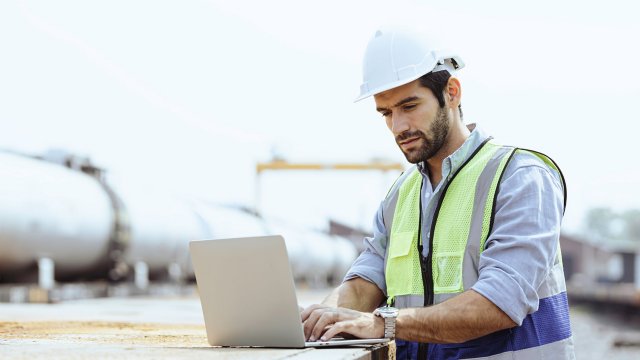 man wearing hard hat at pipeline site on laptop