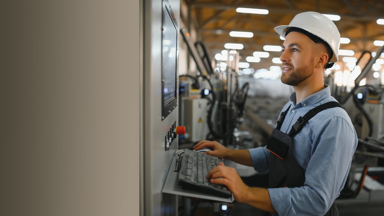 Produktionsmitarbeiter mit Schutzhelm an einem Computer im Fertigungsbereich