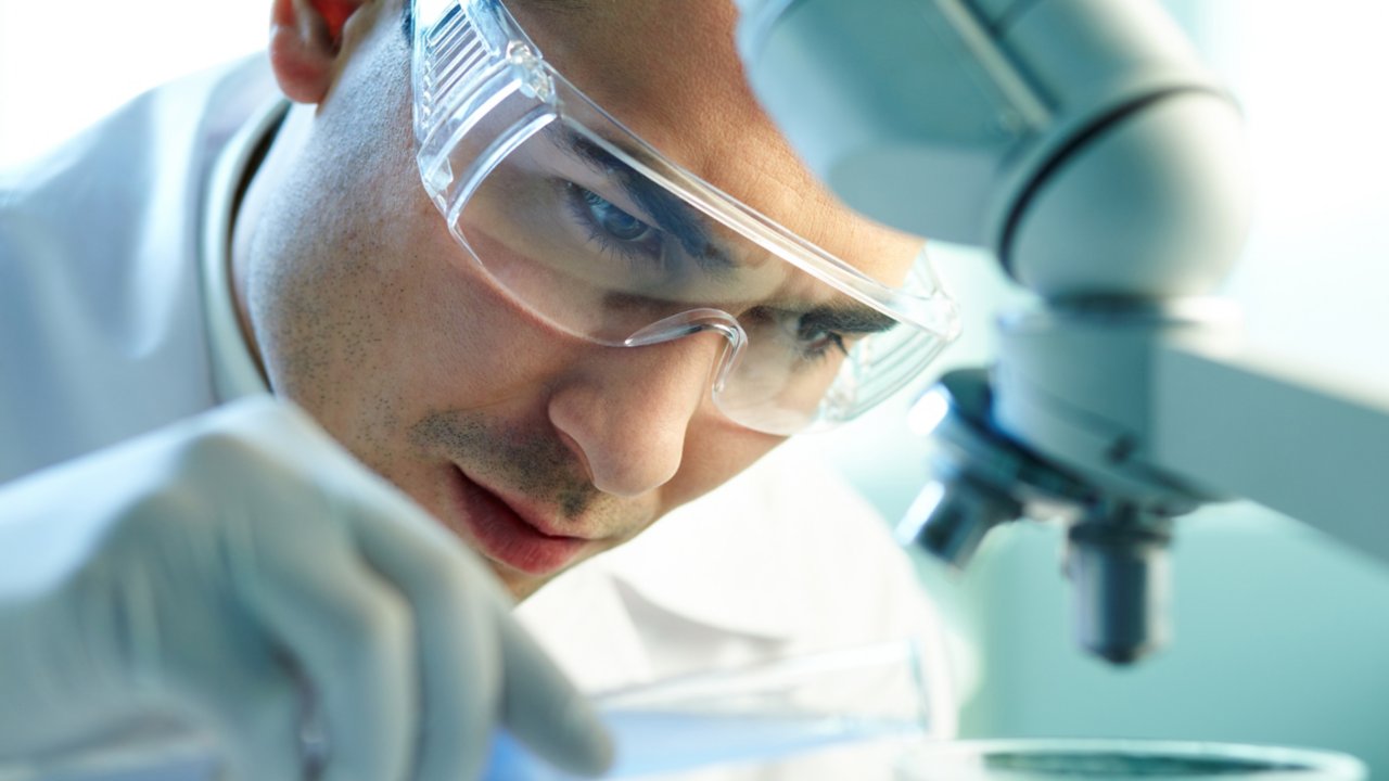 Man in lab wearing safety goggles using microscope