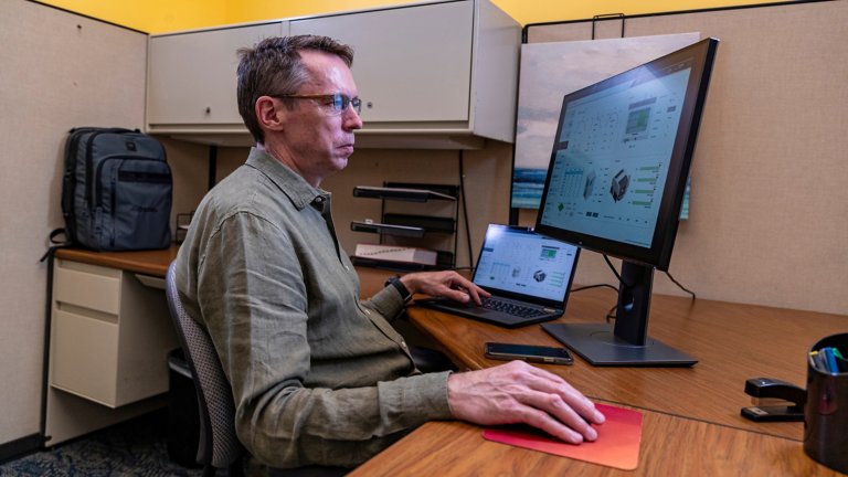 A man sitting at a cubicle desk using modern HMI tools on a computer.