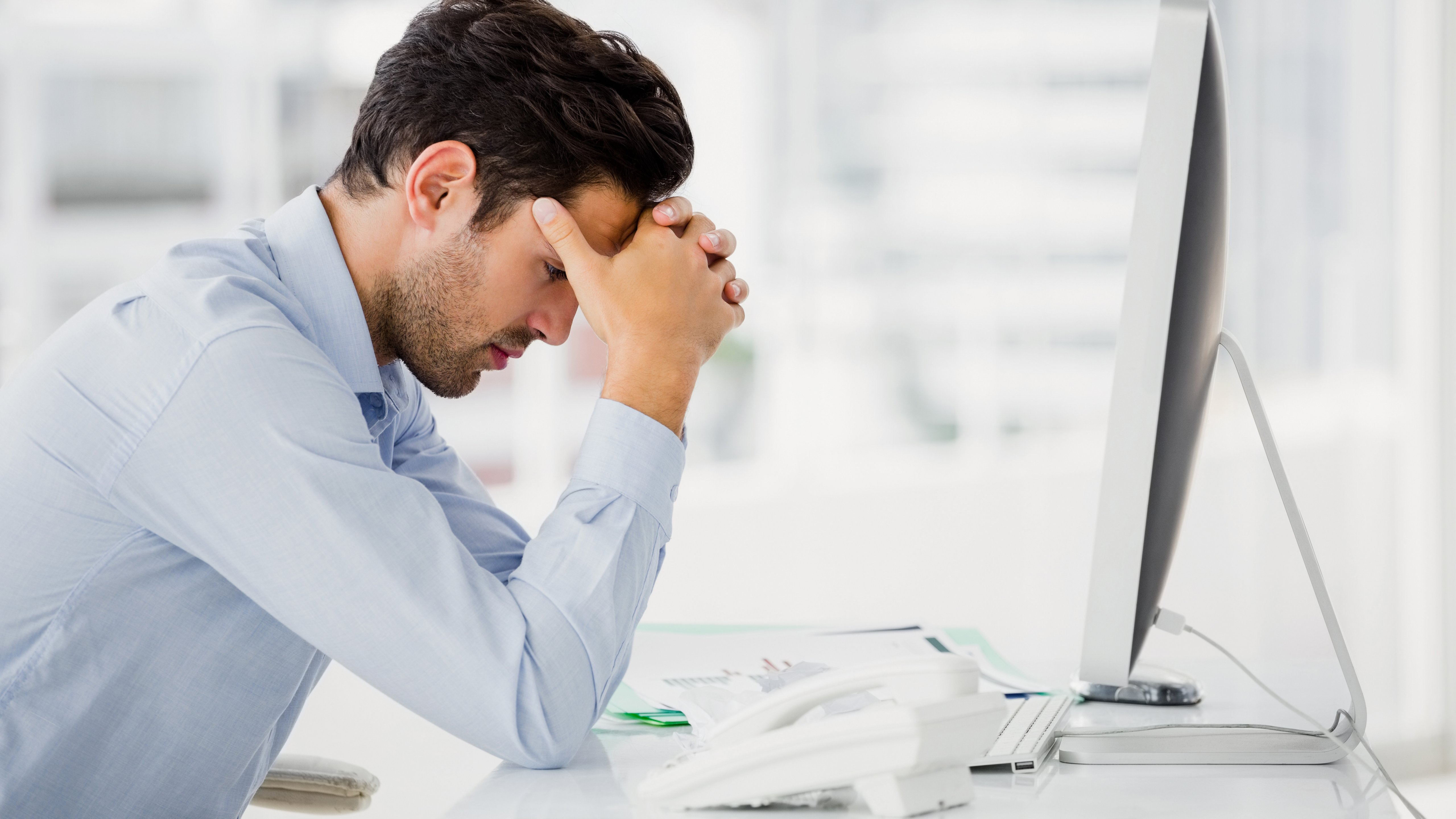 Man sitting at his desk in the office, holding his head with his hands