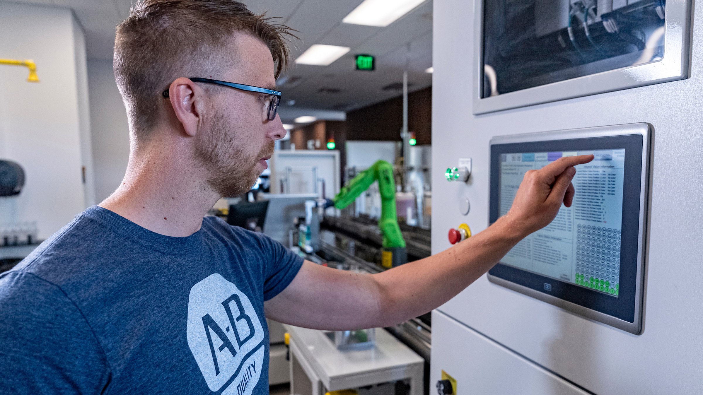 A male operator touching an HMI screen with a green Fanuc collaborative robot in the background. Taken at University of Wisconsin Milwaukee