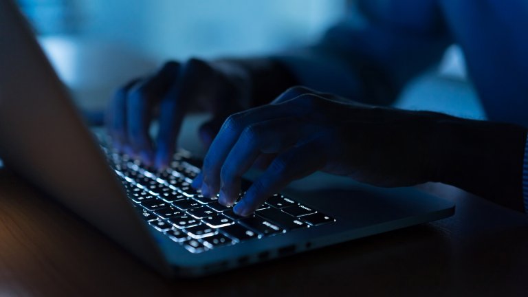 Man typing on laptop keyboard in dark cybersecurity