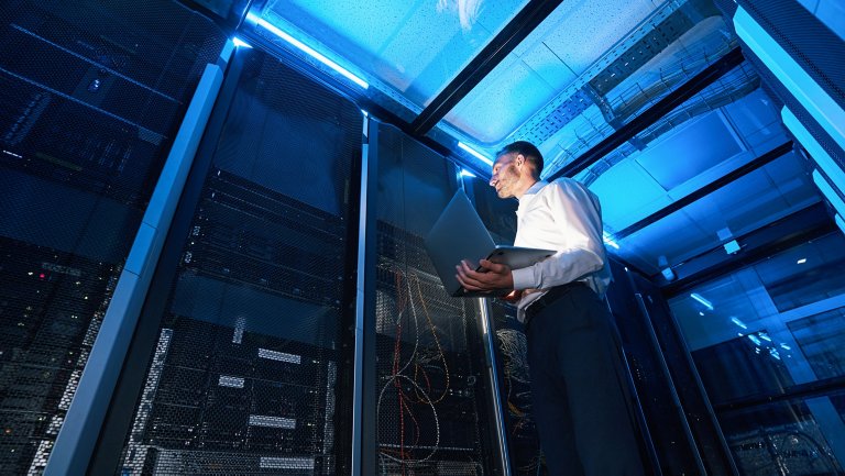 Server administrator of data center with laptop in one hand checking network cabinet