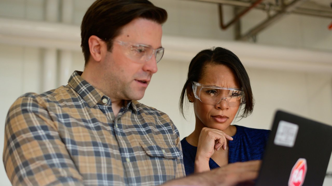 Ein Mann und eine Frau mit Schutzbrillen schauen auf einen Laptop mit Rockwell Automation Logo0119_000430_FactoryTalkAutomation-0480