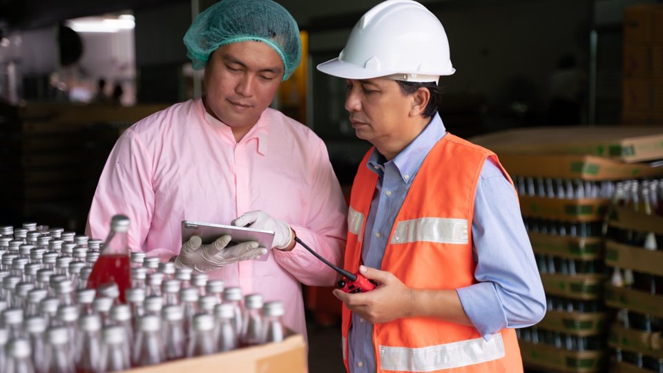 Asiatischer Manager und Mitarbeiter überprüfen die Lebensmittelqualitätskontrolle im Werk mit einem digitalen Tablet