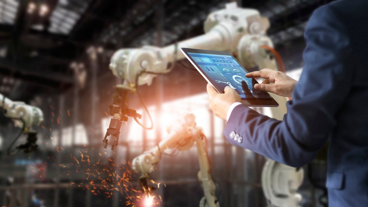 タブレットを使いリアルタイム･モニタ･システム･ソフトウェアでインテリジェントな工場産業のオートメーション･ロボット･アーム･マシンを確認、制御している男性。