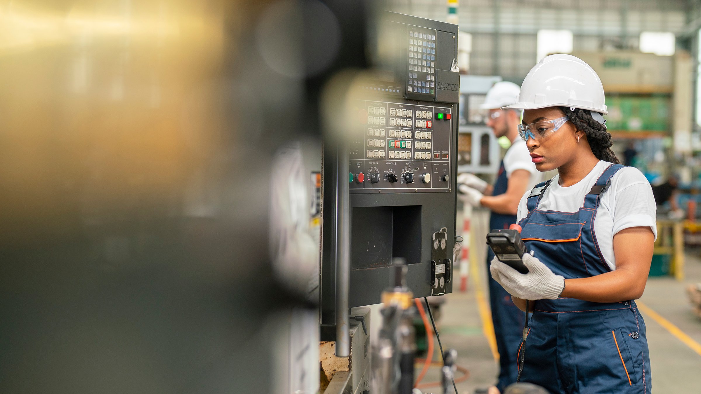 Female apprentice engineer working with CNC machine in factory