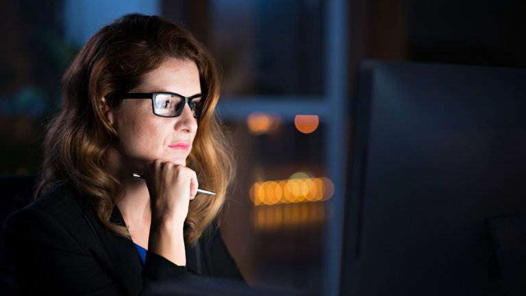 Geschäftsfrau mit Brille, die Informationen auf leuchtendem Computer-Bildschirm liest.