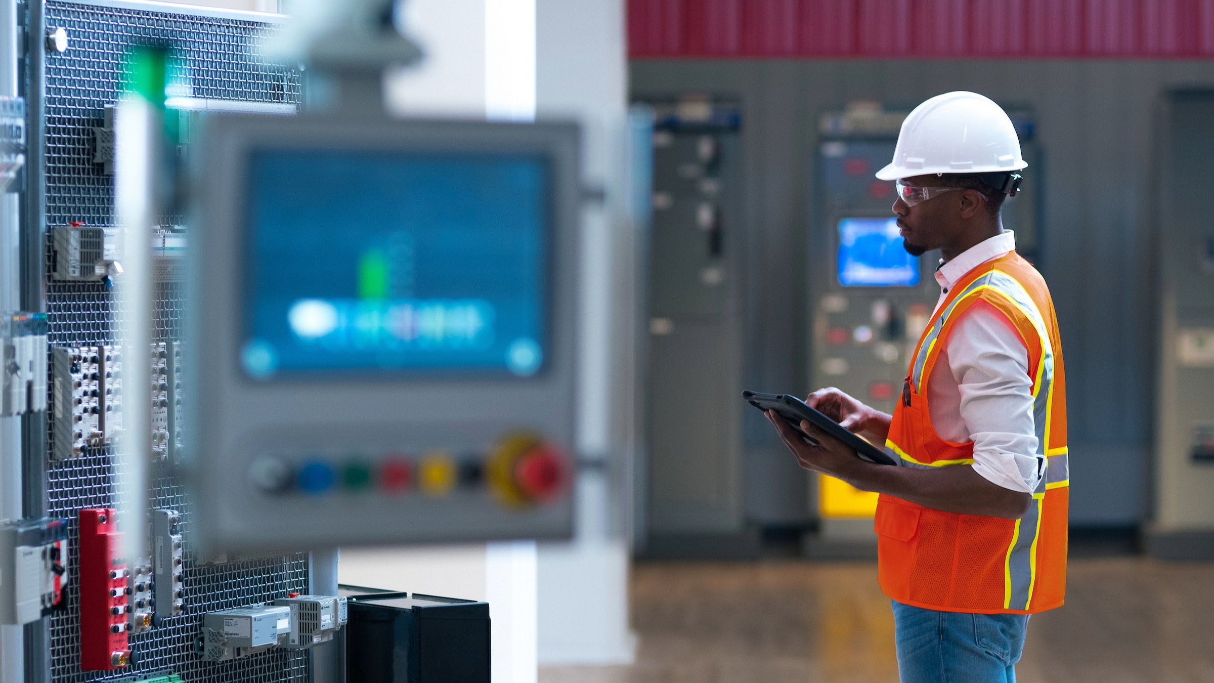 Manufacturing employee on the plant floor holding a tablet and looking at a computer monitor