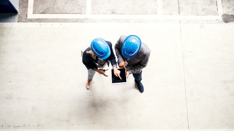 Vista dall’alto di due tecnici industriali (uomo e donna) con un tablet, al lavoro in una fabbrica. Copia spazio.