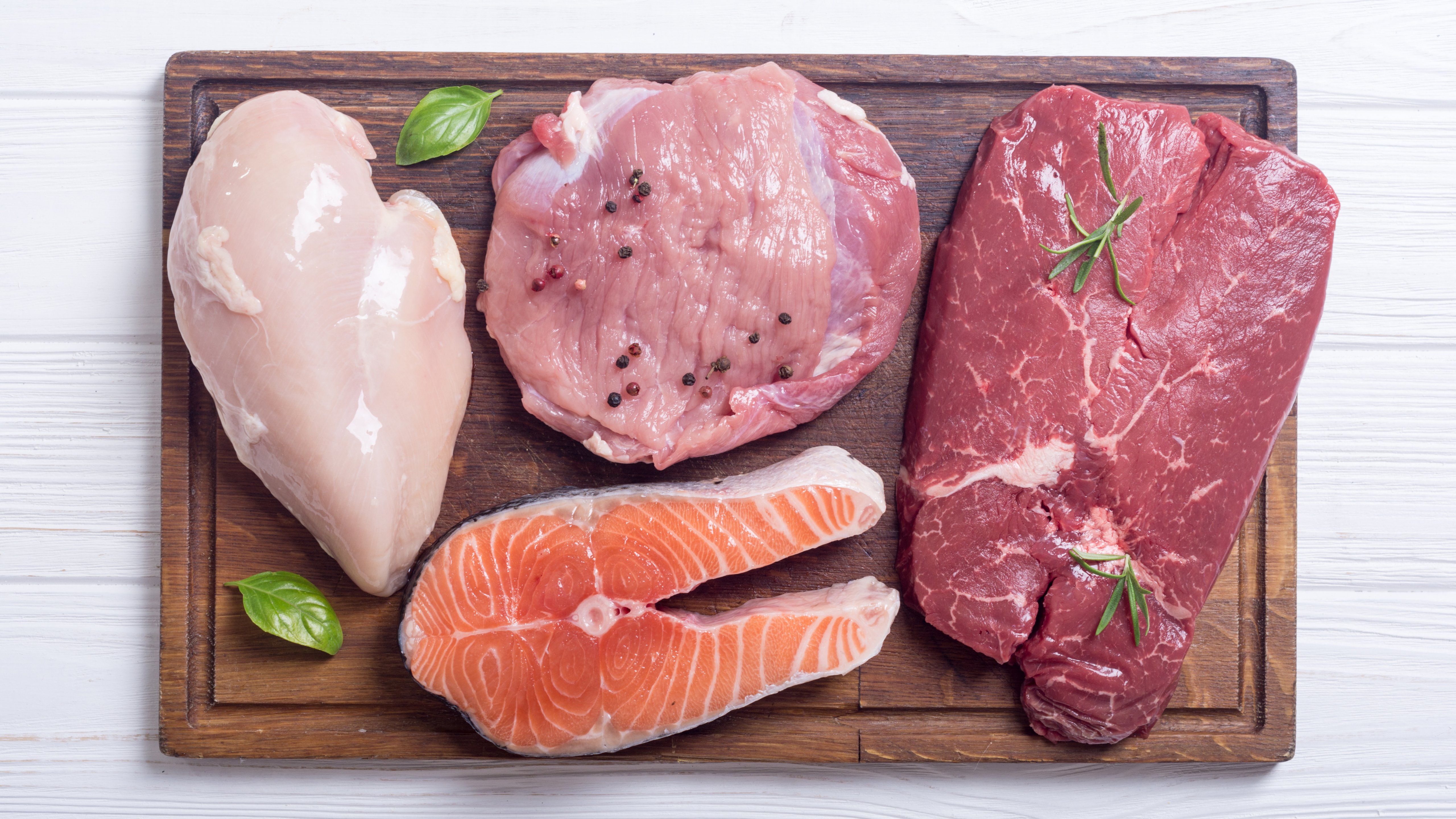 Slices of chicken, salmon, beef and pork freshly cut and sitting on a cutting board. 