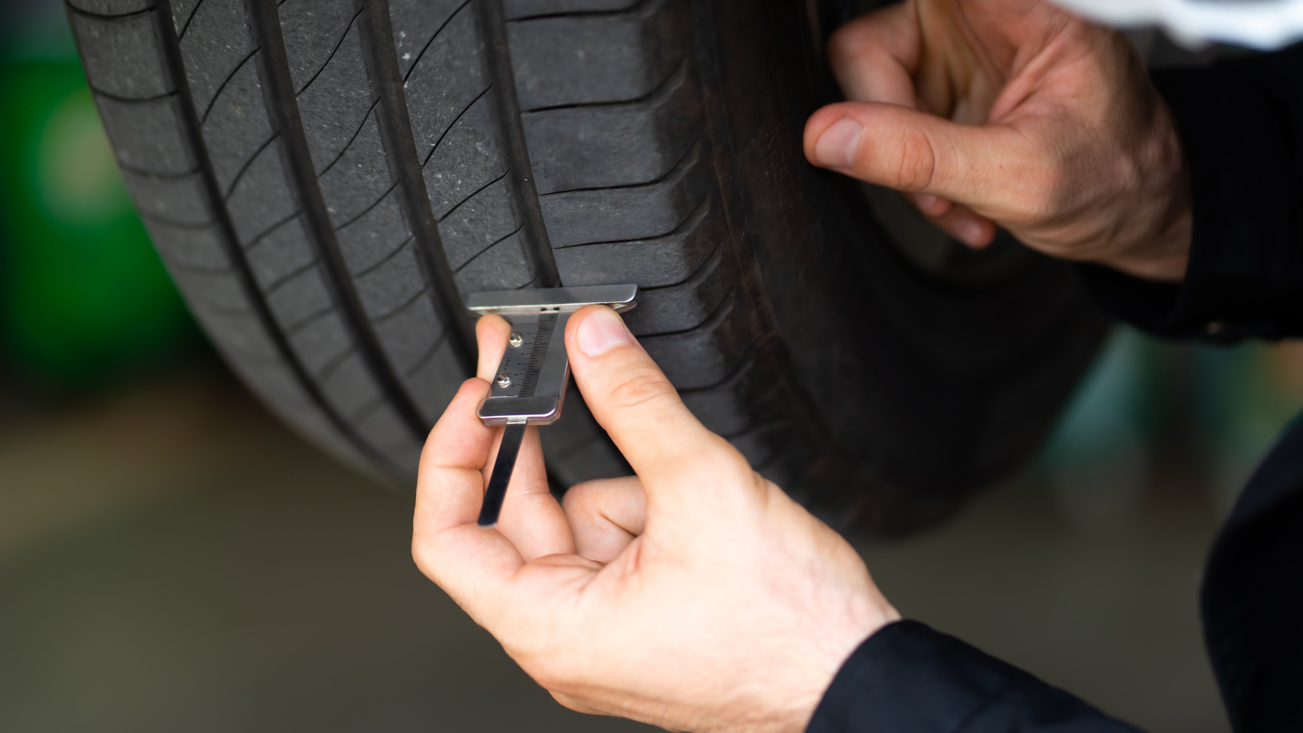 Mechanic checking checking the depth of car tire tread.  Car maintenance and auto service garage concept.