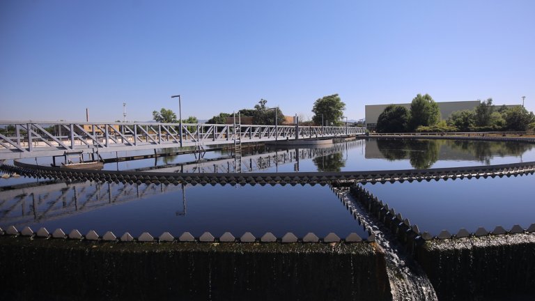Front view of industrial waste water treatment tank with a clear blue sky and offices and trees in the background
