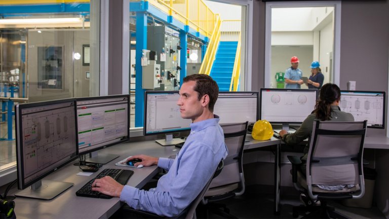 A white male sitting in a control room with multiple computer screens in front of him sitting at his desk.