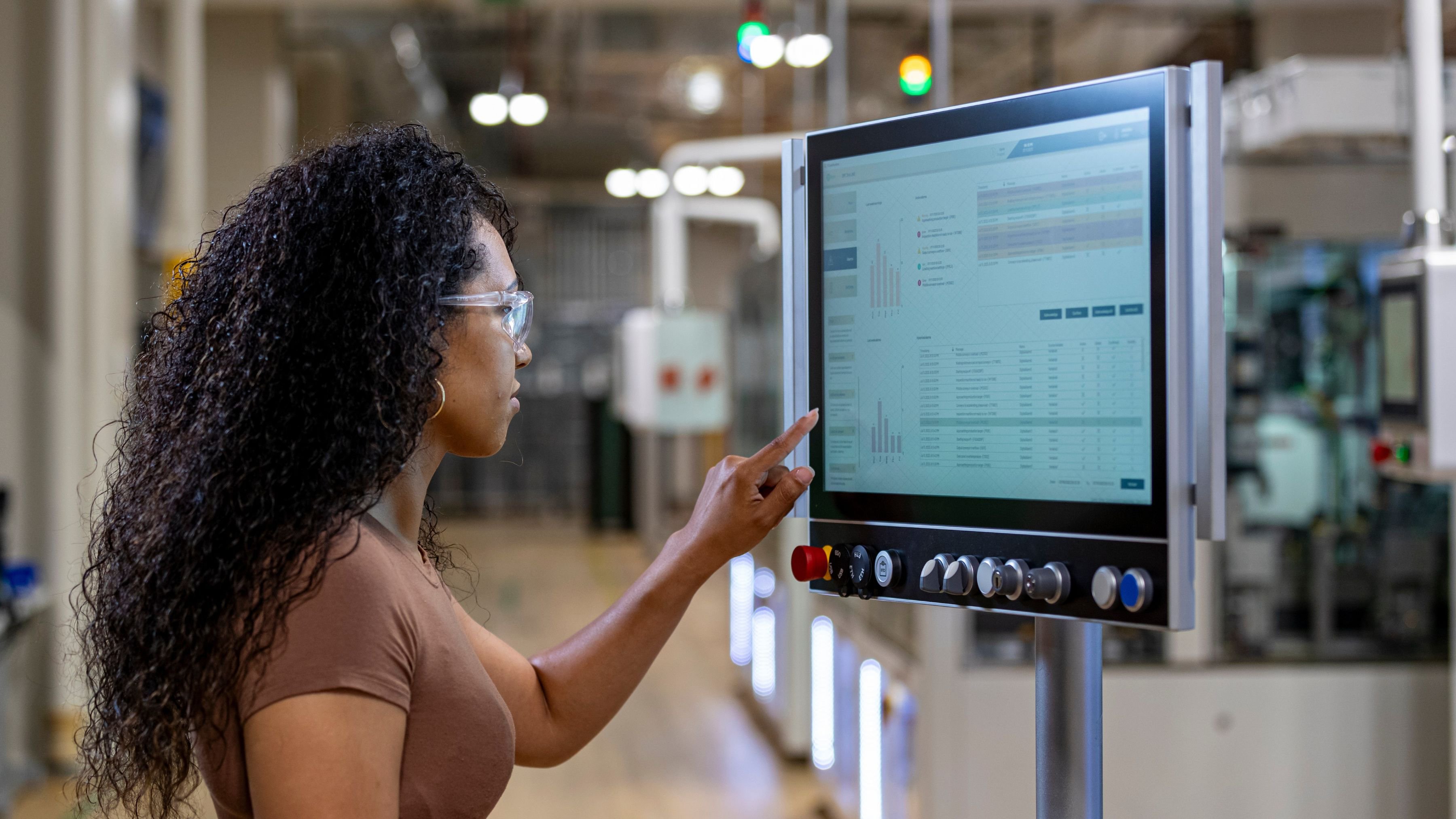 A female operator in front of a smart manufacturing line reaching towards an On-Machine HMI