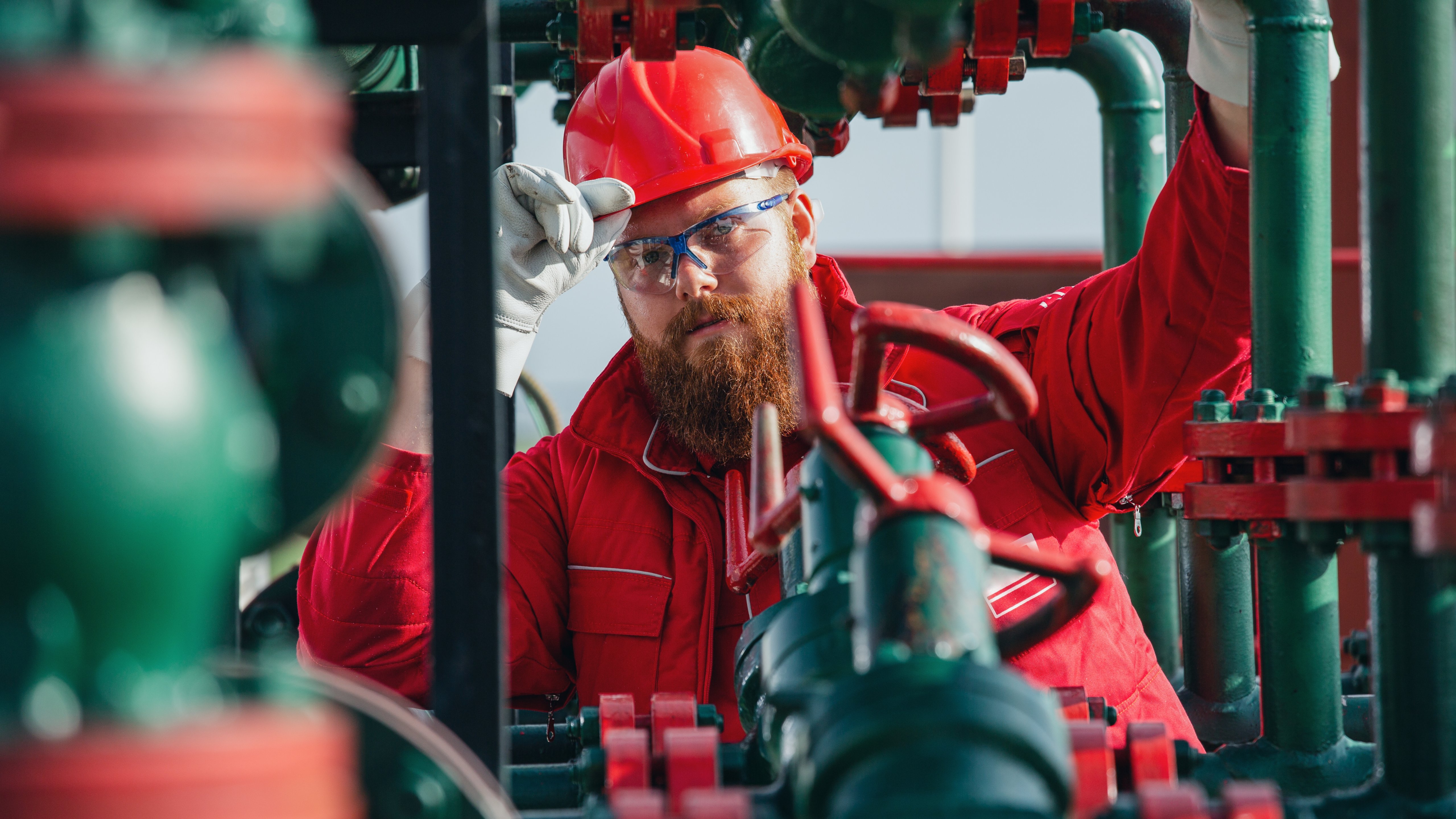 Oil and gas engineer in red jumpsuit working on pipeline equipment. 