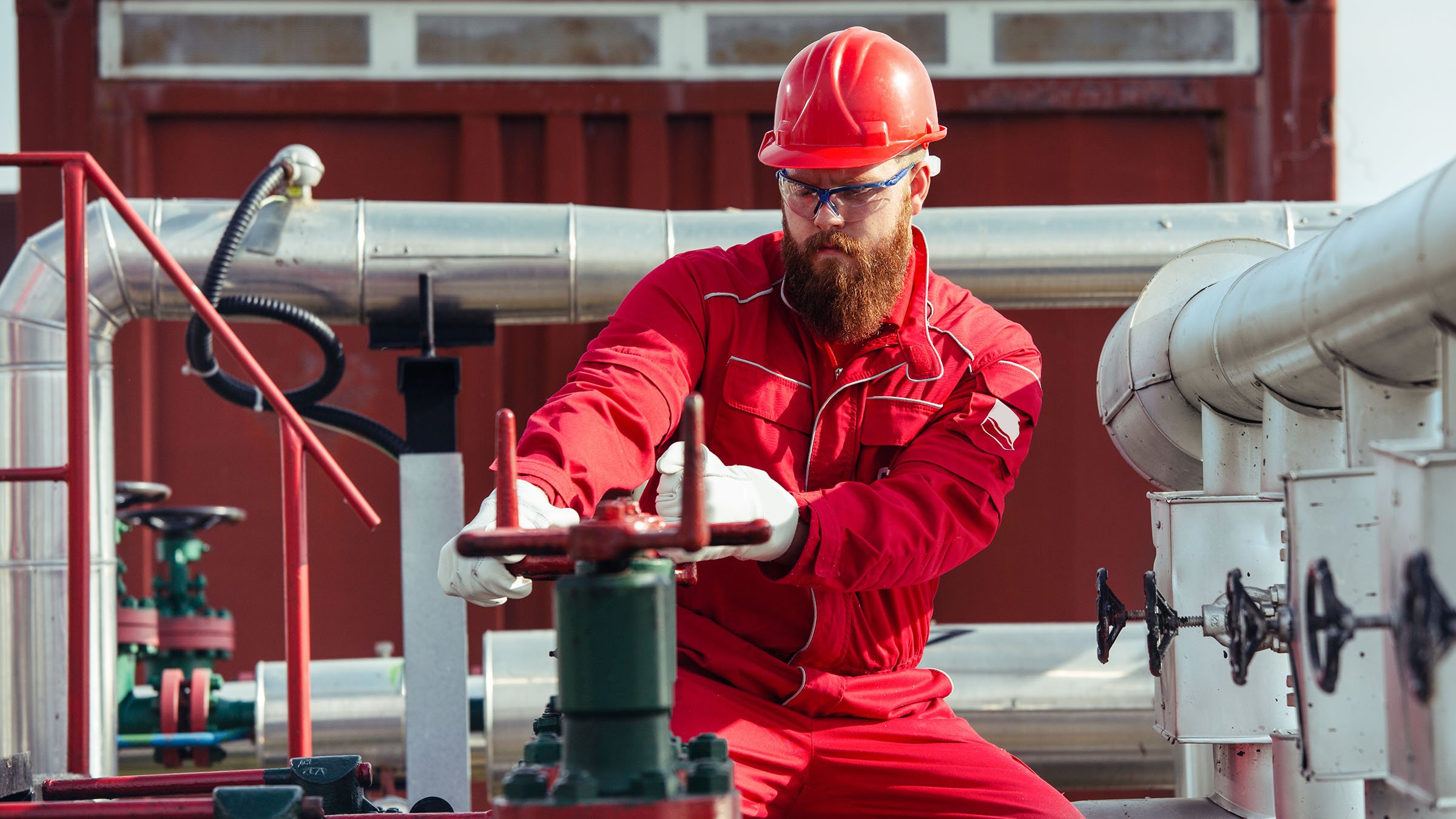 Arbeiter in der Pumpenstation einer Ölraffinerie mit rotem Schutzhelm und Uniform öffnet Pipelineventile. 