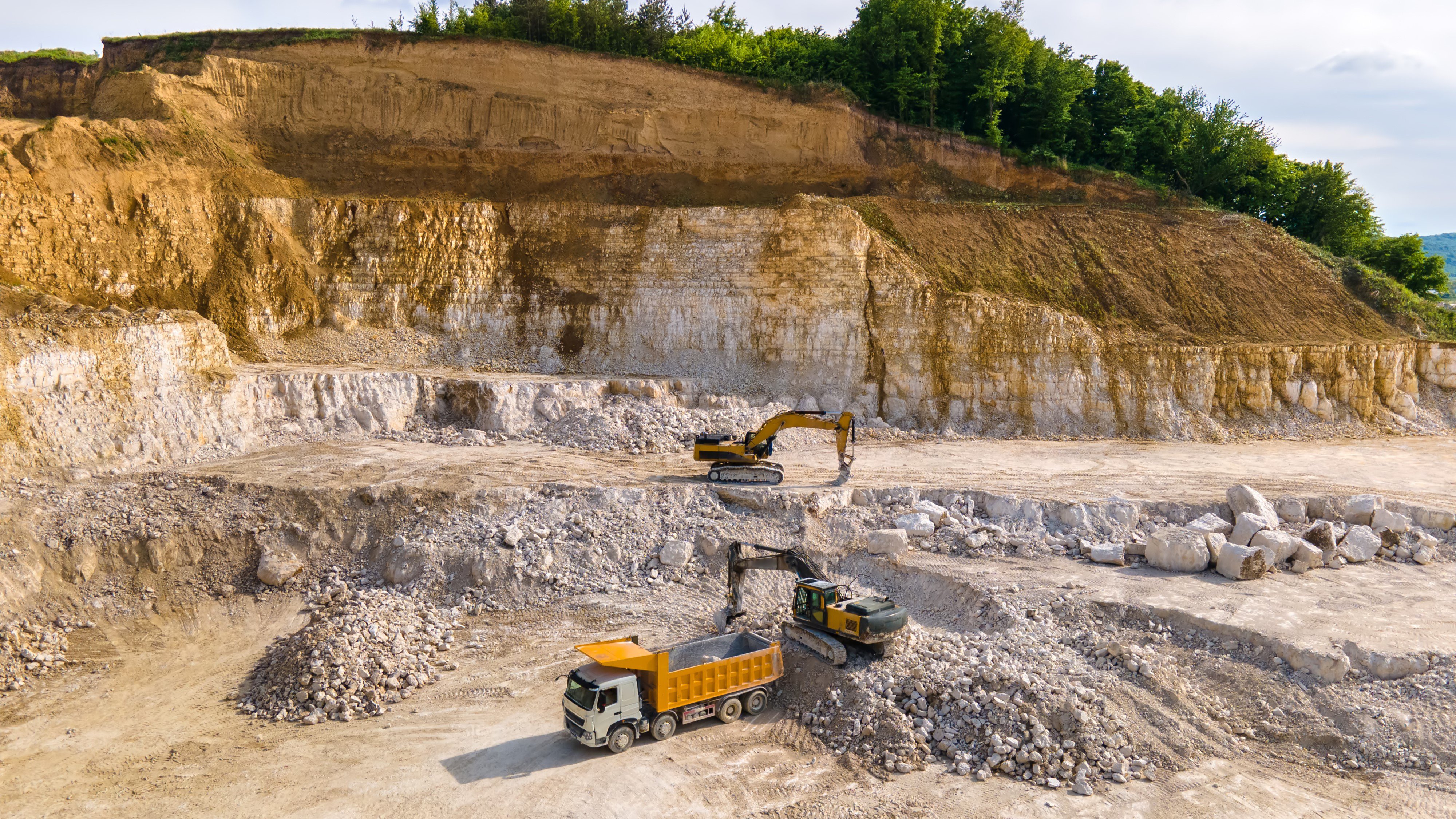 Open pit mining of construction sand stone materials with excavators and dump trucks.